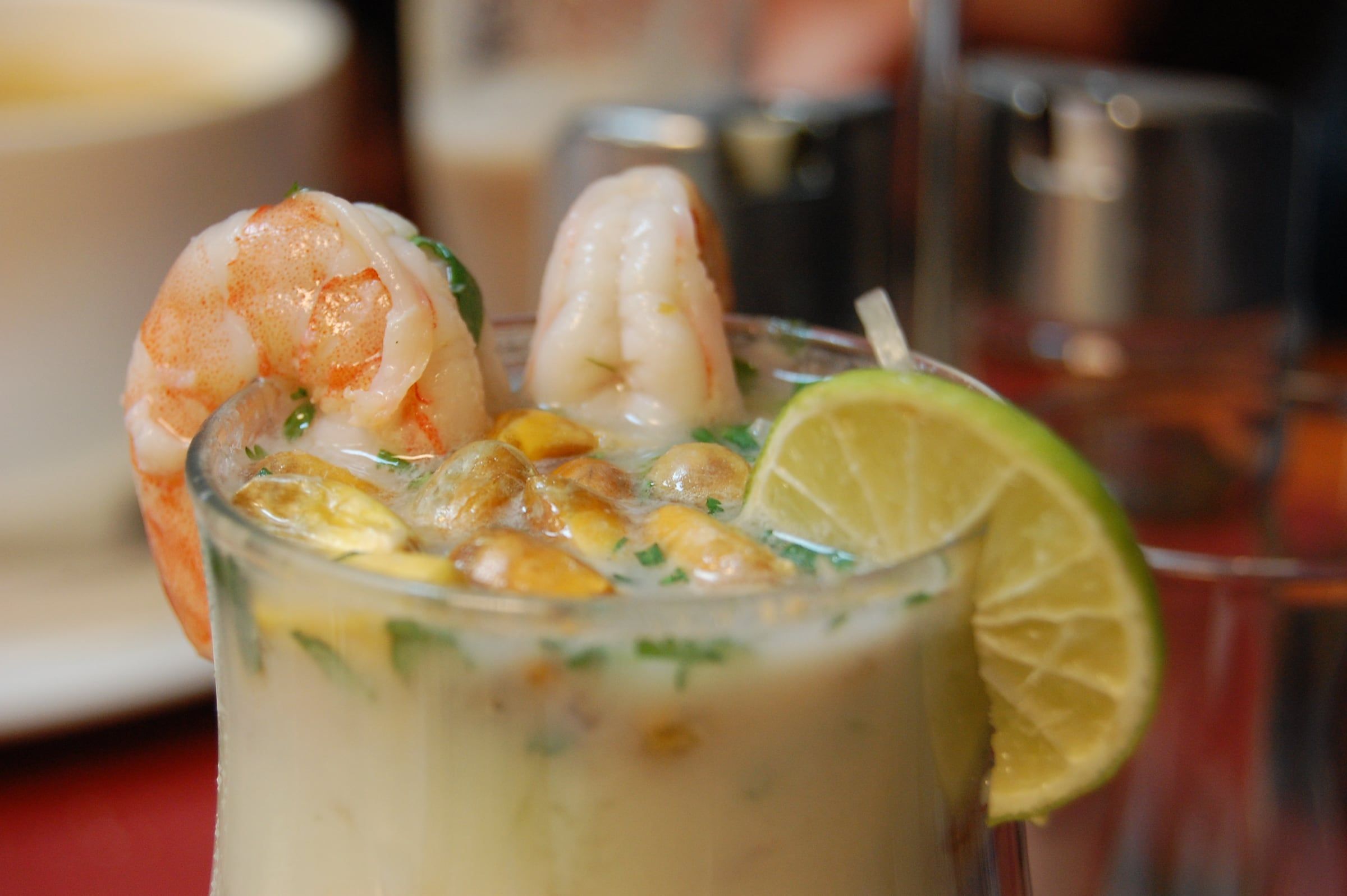Vaso de leche de tigre con langostinos, cancha y una rodaja de limón
