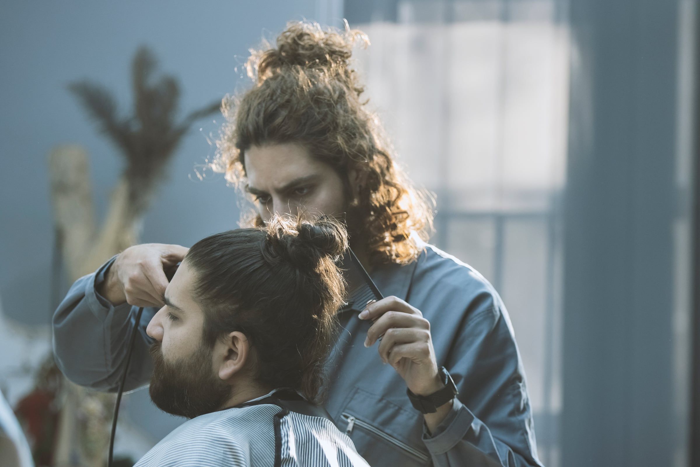Barbero pasando la máquina a un cliente con moño y barba