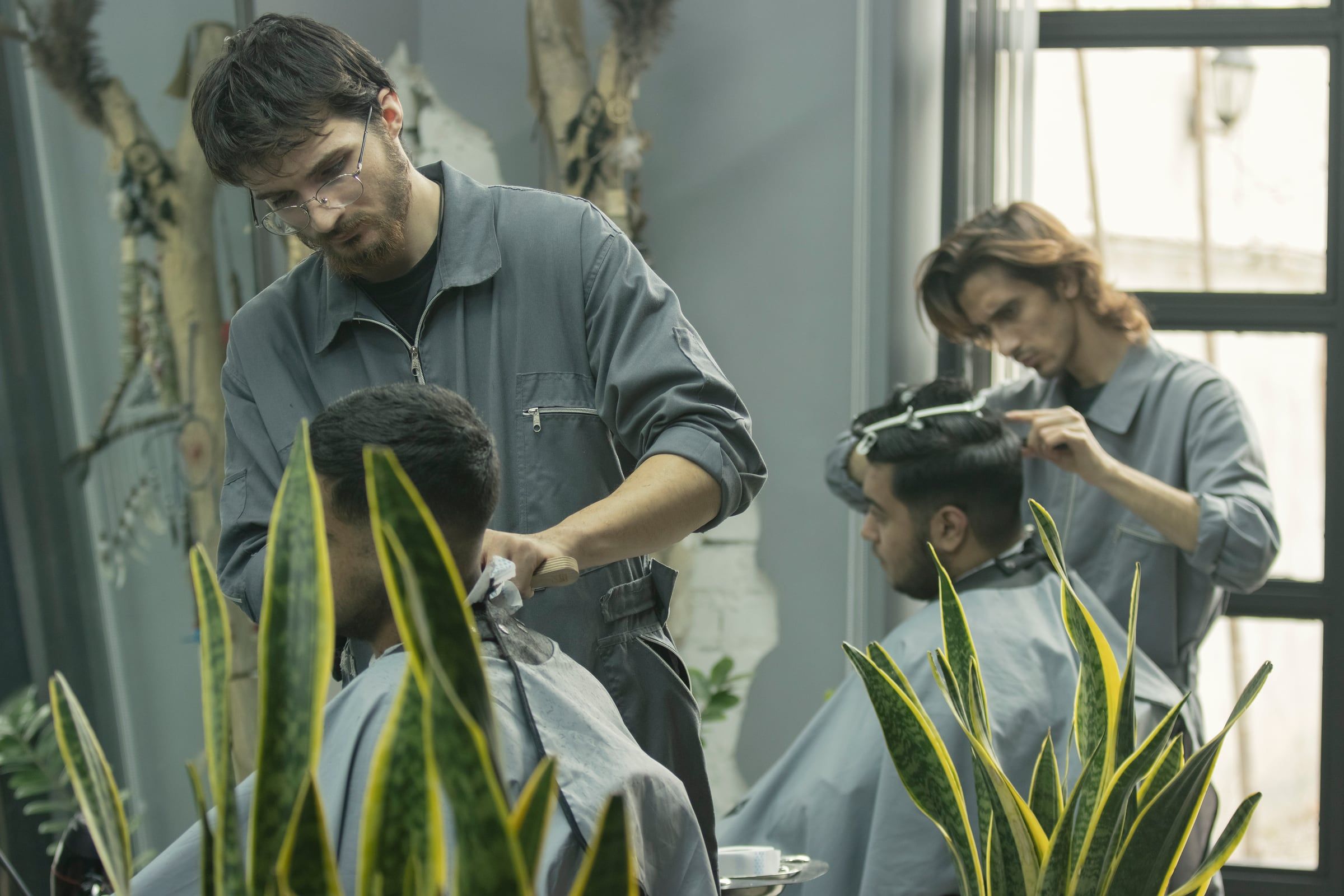 Dos barberos cortando el cabello a sus clientes en una barbería luminosa